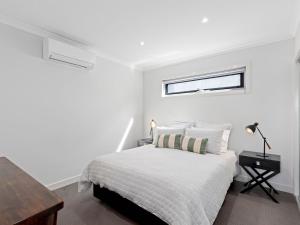 a white bedroom with a bed and a desk at Time Out on Flinders in Indented Head