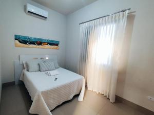 a white bedroom with a bed and a window at Loft 02 - Alvares machado in Álvares Machado
