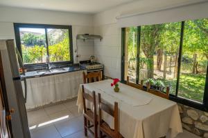 a dining room with a table and a kitchen with windows at Cabaña Piedra y Sol de CACHI in Cachí