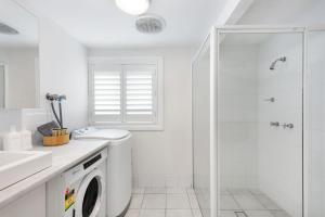 a white bathroom with a washing machine and a shower at Blue View Gerringong in Gerringong