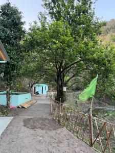 a fence with a green flag next to a tree at Luvyash Campsite Stays in Bhīm Tāl