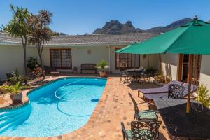 a swimming pool with a green umbrella and chairs at Hout Bay Lodge in Hout Bay