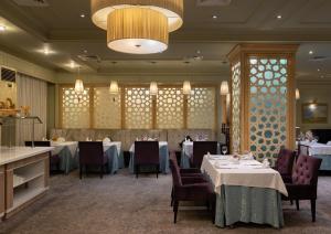 a dining room with tables and chairs and a chandelier at Grand Tien Shan Hotel in Almaty