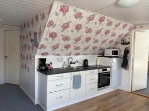 a kitchen with white cabinets and pink flowers on the wall at Tante Jannis Sommerpension in Bogense +16 photos