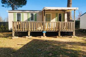 a small yellow house with a porch and a tree at Mobil home 3 chambres - Homair parc des 7 fonts 3 étoiles in Agde