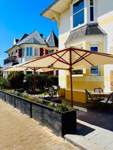 a patio with tables and umbrellas in front of a building at Bed & Breakfast Maison Noire Westende-bad incl parking & ontbijt in Middelkerke