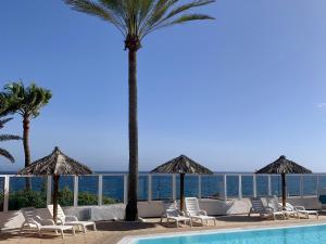 a pool with chairs and palm trees and the ocean at Bungalow Atlantic View in Maspalomas
