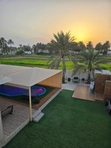 an outdoor patio with a large white umbrella and palm trees at Katara Garden in As Suwayq