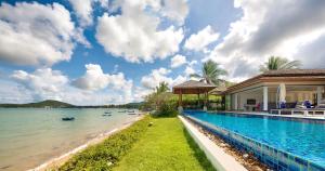 a swimming pool next to a house next to a body of water at Dhevatara Residence Beachfront Villas in Mae Nam