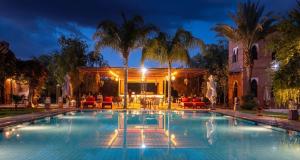 a pool at night with palm trees and chairs at Villa Thaifa & SPA in Marrakesh