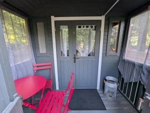 a porch with red chairs and a table and a door at Roulotte enchantée in Cornillé-les-Caves
