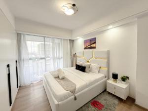 a white bedroom with a large bed and a window at Homly Stays in Kisii