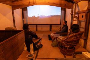 a group of people sitting in a room with a large window at 淵明庵 in Fujikawa