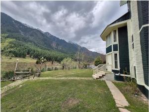 a house with a grassy yard next to a mountain at The Pinus Resort in Pahalgām