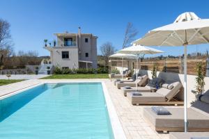 a pool with chairs and umbrellas next to a house at Villa Kouros P&A in Áfra