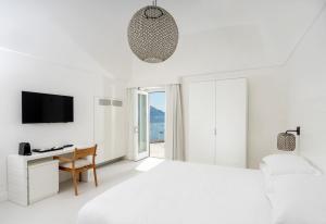 a white bedroom with a bed and a desk and a tv at Hotel Posa Posa in Positano