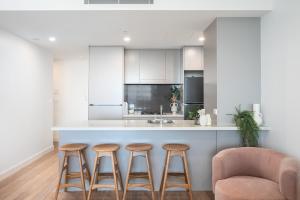 a kitchen with three bar stools and a counter at 1011 - First Light 2BR with Ocean Views - Prime Location in Newcastle