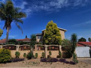 a fence in front of a house with a palm tree at Emakhaya B&B in Mthatha