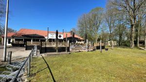 a building with a fence and a grass field at Geniet van rust en privacy in onze gezellige chalet op familiecamping De Tien Heugten in Drenthe in Schoonloo