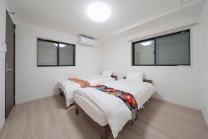 two beds in a room with white walls and windows at the UNIT5 HOUSE Roppongi in Tokyo