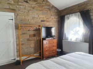 a bedroom with a bed and a tv and a brick wall at Edgerton cottage, large 1-bed detached coach house in town, Spacious rustic charm in Lindley +11 photos