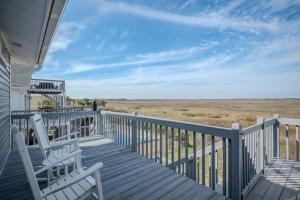 a deck with two chairs and a view of a field at Late For The Sky in Caswell Beach