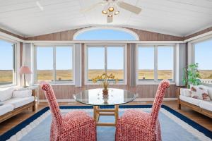 a living room with a table and chairs and windows at Late For The Sky in Caswell Beach