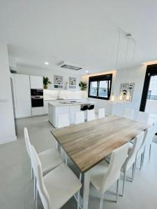 a large white kitchen with a wooden table and white chairs at Lujosa casa en primera línea playa increibles vistas mar in Laredo