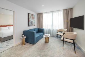 a hotel room with a blue couch and a bed at Dorsett Hotel Canary Wharf in London