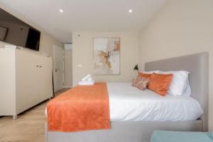 a bedroom with a large white bed with an orange blanket at Calvário Suites l in Chaves