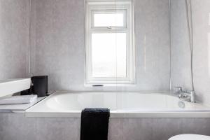 a white bathroom with a tub and a window at 3 Bedroom House By Cozy Quarters Property Management Contractors Accommodation Seaham Near Sea in Seaham +21 photos