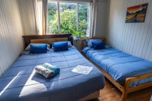 two beds in a room with blue sheets and a window at Hostal refugio nomada in Puerto Montt