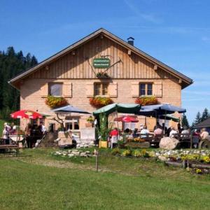 um edifício com mesas e guarda-chuvas à sua frente em Jausenstation Neuschwand em Hittisau