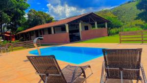 a swimming pool with two chairs and a house at Tríade Chalé da Canastra 2 in São Roque de Minas