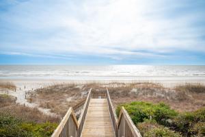 a wooden staircase leading to a beach with the ocean at Captains Choice by Oak Island Accommodations in Caswell Beach