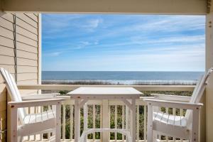 a porch with two chairs and a table and the ocean at Captains Choice by Oak Island Accommodations in Caswell Beach
