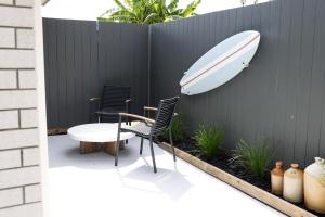 a surfboard attached to a fence with two chairs and a table at Coastal Calm Papamoa in Tauranga