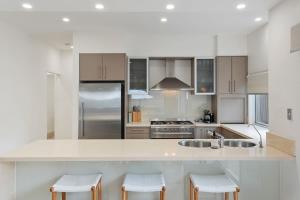 a white kitchen with a counter and stools at Pet Friendly Modern Oasis with Private Pool in Noosaville