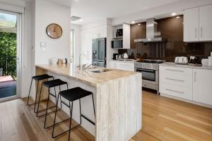 a kitchen with white cabinets and a large island with bar stools at Modern airy duplex steps to River heated pool in Noosaville +13 photos