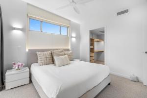 a white bedroom with a large bed and a window at Spacious 4-Bed Coastal Home with Pool in Mooloolaba