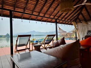 a patio with chairs and a table and a view of the water at D Hostel by the river in Kanchanaburi City