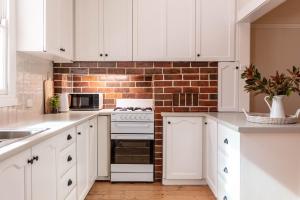 a kitchen with white cabinets and a brick wall at Central 3BR Heritage Home Walk to Sovereign Hill & CBD Free Parking in Ballarat