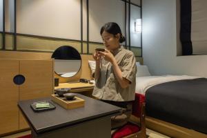 a woman in a hotel room looking at her cell phone at Mitasuya Ryokan Hotel by Anook Gwangju in Gwangju +183 photos