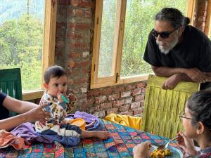 a baby sitting at a table eating food with two people at Nomad Eco Retreat in Shimla