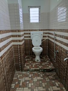 a tiled bathroom with a toilet and a window at Cloud Hill Homestay in Jālāpahār