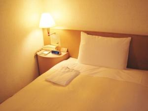 a bedroom with a white bed with a lamp and a phone at Urban Hotel Twins Chofu in Chofu