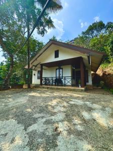 a small white house with a porch and trees at Wind Bells in Anaviratty