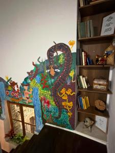 a painting of a dragon on a wall next to a book shelf at Helin's Hostel in Berat