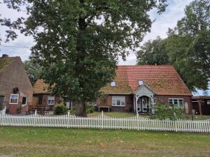 a white fence in front of a house with a tree at Entspannen auf der Old Charmi Ranch in Kutenholz