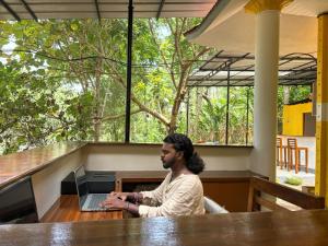 a man sitting at a table with a laptop computer at Hope Hostels - Munnar in Munnar